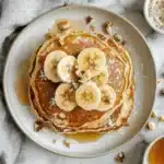 Cottage Cheese Banana Pancakes That Taste Like a Weekend Treat 6 Top-down view of pancakes with banana slices and crushed nuts on a plate