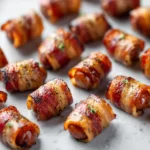 Bacon-wrapped sausage bites arranged on a baking sheet, evenly browned and lightly seasoned.