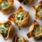 Top view of baked spinach artichoke wonton bites with lightly browned edges on a white surface.