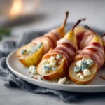 Smoked turkey-wrapped pear halves on a plate, topped with blue cheese crumbles and softly lit in a cozy setting.