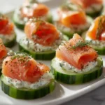 Cucumber slices topped with herb cream cheese and folded smoked salmon arranged neatly on a serving tray.