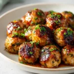Plate of golden sweet chili chicken meatballs with caramelized edges and fresh herbs sprinkled on top.
