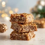 Stack of gingerbread oat bars on a light surface with soft golden holiday lights in the background.