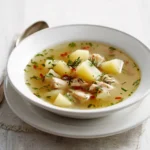Quick Chicken & Potato Soup 3 Bowl of chicken and potato soup with herbs and diced vegetables on a white table setting.