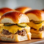 Close-up of cheeseburger sliders with melted American cheese, pickles, and soft golden buns on a wooden board.