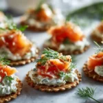 Multiple smoked trout and dill cream cheese crispbread bites arranged on a light surface with fresh herbs.