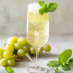 New Year’s Sparkling White Grape Mocktail 3 A sparkling white grape mocktail in a flute with mint and grapes, bright natural light and fresh grapes in the background.