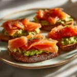 Smoked salmon and avocado crostini served on a ceramic plate in warm natural light.