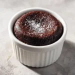 Chocolate Lava Cakes for Two 3 Single baked chocolate lava cake in a white ramekin, topped with a light dusting of powdered sugar on a neutral surface.