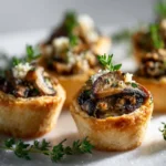Mushroom & Thyme Tartlet Bites 3 Close-up of a golden mushroom tartlet topped with sautéed mushrooms and thyme sprigs.