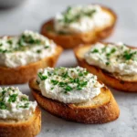 Whipped Ricotta Crostini with Roasted Cherry Tomatoes 3 Crostini topped with whipped ricotta and fresh chopped herbs on a light surface.
