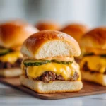 Cheeseburger sliders stacked on a wooden serving board with glossy buns, melted cheese, and pickles in warm light.