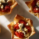 Overhead view of roasted red pepper and feta phyllo cups arranged on a marble surface with golden flaky edges.