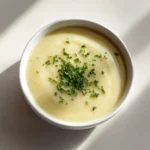 Quick Potato & Leek Soup 3 Top-down view of creamy potato and leek soup in a white bowl, topped with chopped chives on a bright surface.