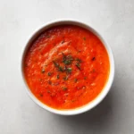 15-Minute Tomato Vegetable Soup 3 Overhead view of smooth tomato vegetable soup in a white bowl on a light neutral surface