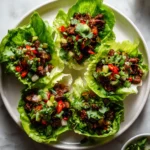 Plate of multiple teriyaki beef lettuce cups arranged in a circle, filled with glossy beef, herbs, and chopped vegetables.