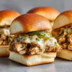Close-up of baked chicken Philly sliders with melted provolone, sautéed peppers, and onions on soft rolls.
