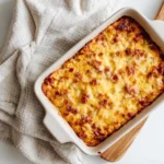 Overhead view of hot Reuben dip with melted cheese and corned beef in a square baking dish on a neutral linen cloth.