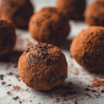 Cocoa-dusted chocolate truffle energy bites on parchment with rich texture and deep chocolate color.