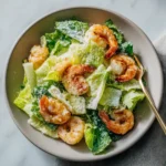 Overhead view of shrimp Caesar salad with seasoned shrimp, romaine lettuce, creamy dressing, and grated Parmesan in a neutral bowl.