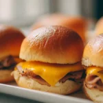 Golden Hawaiian sliders filled with sliced turkey and melted cheese, lined up on a white platter in soft natural light.