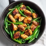 Skillet Chicken Breast with Green Beans 3 Top-down view of cast iron skillet filled with bite-size chicken breast pieces and bright green beans, lightly browned and seasoned.