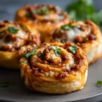 Sausage pizza pinwheels garnished with herbs on a dark plate with soft natural lighting.