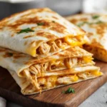 Stacked mini chicken quesadillas cut open to show shredded chicken and melted cheese on a wooden board.