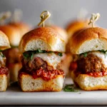 meatball sub sliders with marinara, melted cheese, and fresh herbs secured with toothpicks on a white platter
