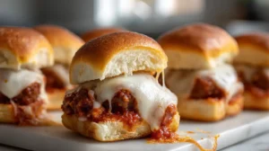 meatball sub sliders with melted mozzarella and marinara sauce on soft rolls arranged on a serving board