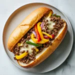 ground beef philly cheesesteak with bell peppers and onions on a hoagie roll served on a white plate
