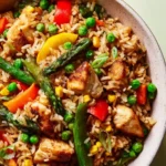 Spring Chicken Fried Rice with Veggies 3 Close-up of chicken fried rice with peas, corn, asparagus, and red bell peppers in a ceramic bowl.