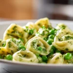 Creamy pesto tortellini with peas served on a white plate, glossy green sauce coating the pasta in soft natural light