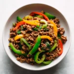 Ground beef and bell pepper stir fry served in a white bowl with red, yellow, and green peppers.