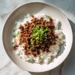 Top-down view of Korean ground beef over white rice with chopped green onions and red pepper flakes in a light ceramic bowl