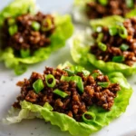Close-up of ground beef lettuce wraps on a light surface, topped with sliced green onions and rich, glossy sauce.
