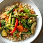 Healthy Spring Veggie Stir-Fry 3 Overhead view of spring vegetable stir-fry with broccoli, carrots, zucchini, and asparagus served over brown rice in a white bowl.