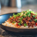 Korean ground beef in a glossy sweet soy sauce served over white rice and topped with sliced green onions in a black bowl
