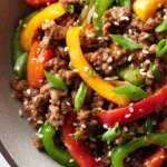 Close-up of ground beef stir fry with red, yellow, and green bell peppers topped with sesame seeds and green onions.