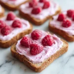 Raspberry Cream Cheese Toasts 3 toasted bread slices spread with pink raspberry cream cheese and fresh raspberries on a light marble surface